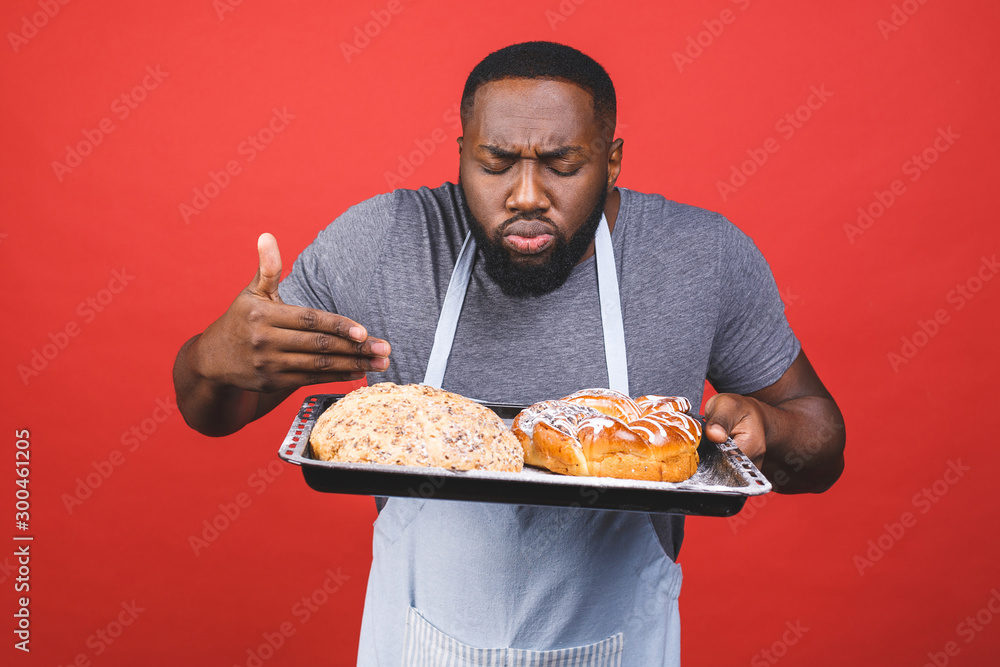 Crazy young african american male chef cook or baker man in striped apron grey t-shirt posing isolated over red background. Cooking food concept. Mock up copy space. Crazy young african american male chef cook or baker man in striped apron grey t-shirt posing isolated over red background. Cooking food concept. Mock up copy space.