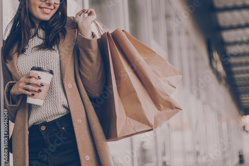 Beautiful fashionable woman drink coffee walking near mall with shopping bags.
