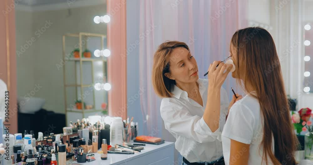Workplace of the makeup artist, a large mirror and a shelf with tools, creams and makeup products. Master paints the eyes of the girl. Workplace of the makeup artist, a large mirror and a shelf with tools, creams and makeup products. Master paints the eyes of the girl.