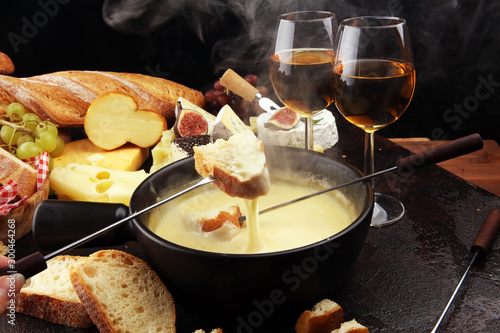 Gourmet Swiss fondue dinner on a winter evening with assorted cheeses on a board alongside a heated pot of cheese fondue with two forks dipping photo