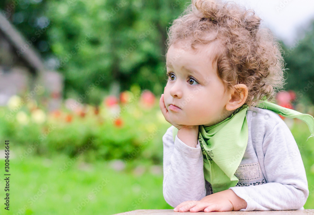little beautiful girl looks thoughtfully into the camera, resting her head on her hand, thinking, imagining something. child in the summer on green background in nature. childhood concept little beautiful girl looks thoughtfully into the camera, resting her head on her hand, thinking, imagining something. child in the summer on green background in nature. childhood concept