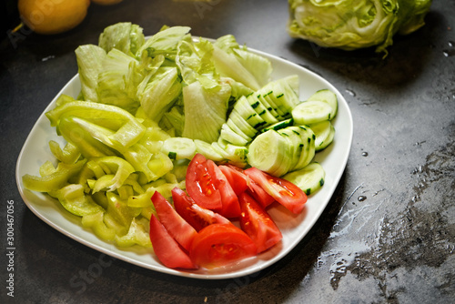 Cut tomatoes, cucumber and iceberg salad on dark kitchen board