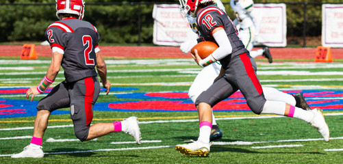 High school football player running with the ball following his blocker