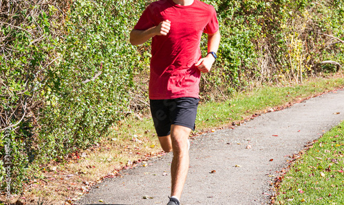Teenage boy running in red shirt on tar path is bright sunlight