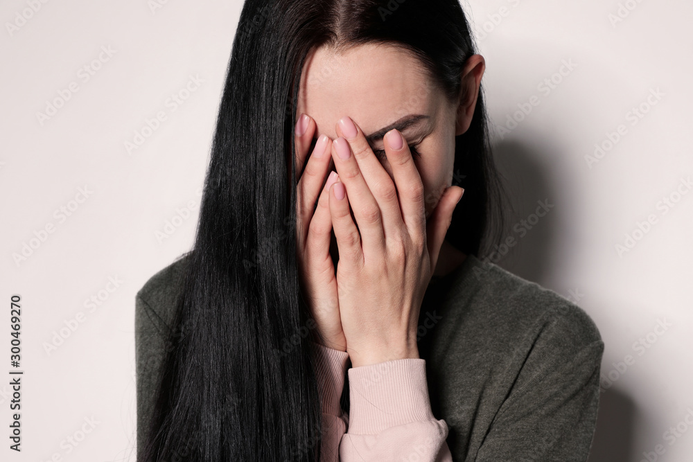 Upset young woman crying against light background Upset young woman crying against light background
