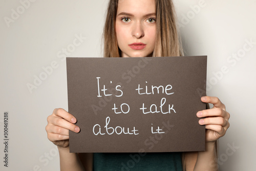 Fotografie Young woman holding card with words IT'S TIME TO TALK ABOUT IT against light bac