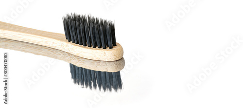 Wooden bamboo toothbrush with black bristles  closeup detail isolated on glossy white table reflection visible   space for text right side