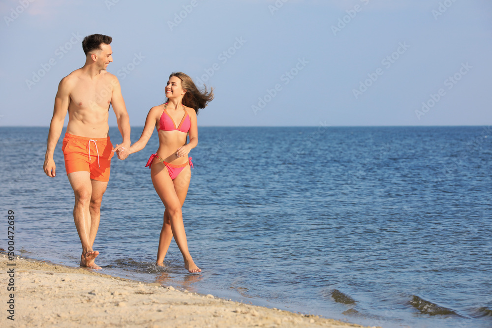 Young woman in bikini spending time with her boyfriend on beach. Lovely couple