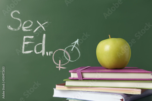 Obraz na plátně Books and apple near chalkboard with phrase Sex ed