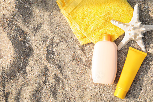 Flat lay composition with bottles of sun protection body cream on sand beach, space for design