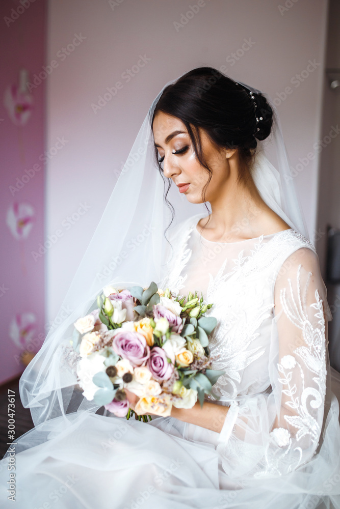 Naklejka premium Stylish happy bride is getting ready in the morning. Happy newlywed woman in bedroom. Beautiful woman with professional make up and hair style. Morning of the bride. Wedding day. Fashion bride.