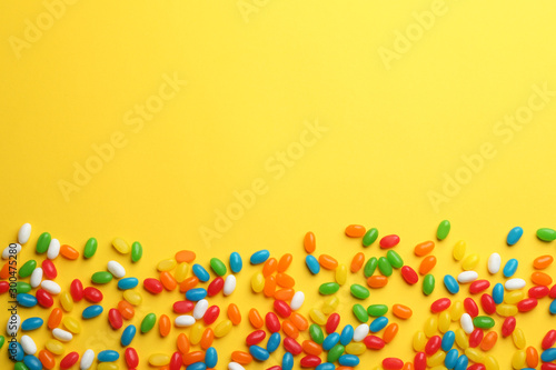 Tasty colorful jelly beans on yellow background, flat lay. Space for text
