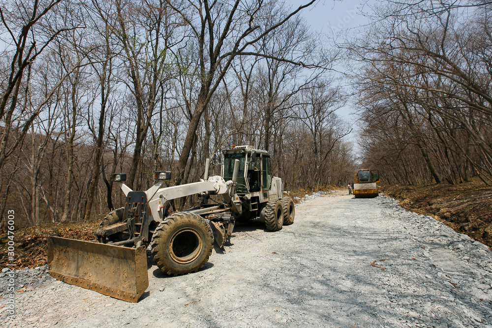 Road construction machinery stands on a dirt road. The construction of a new road in the suburbs. Road construction machinery stands on a dirt road. The construction of a new road in the suburbs.