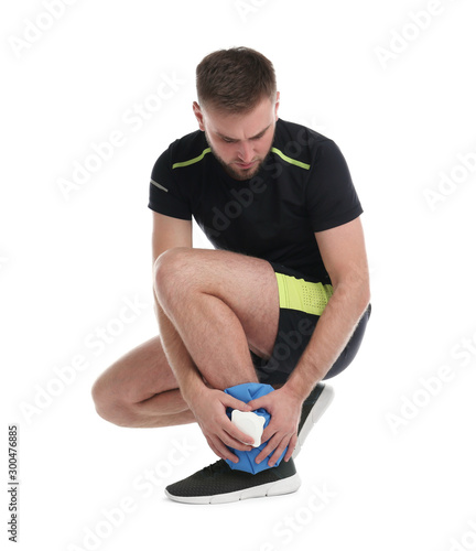 Young man with cold compress suffering from ankle pain on white background