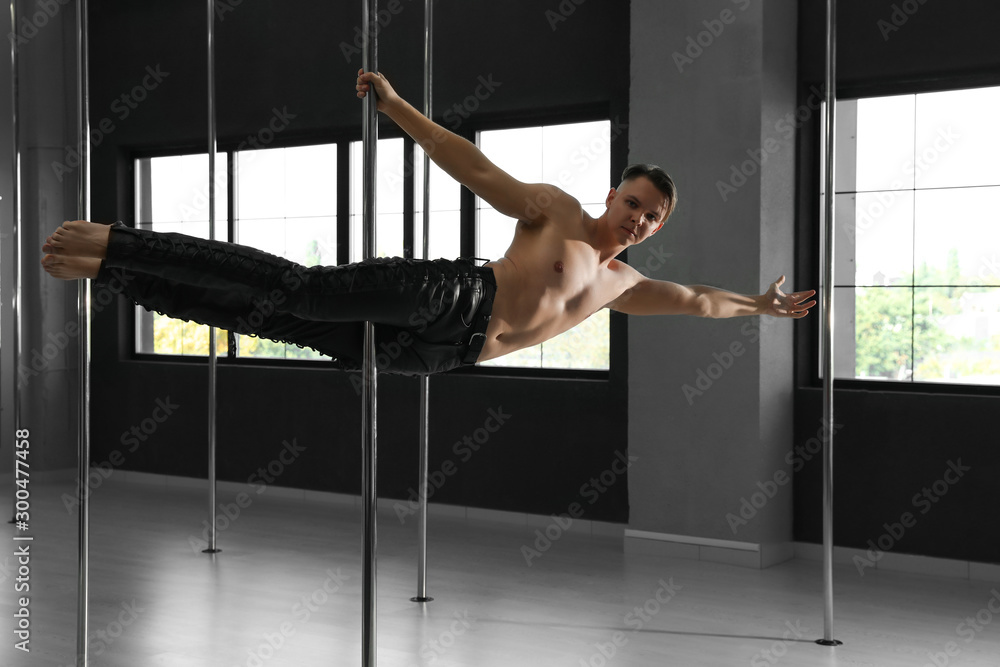 Attractive young man dancing in studio with poles