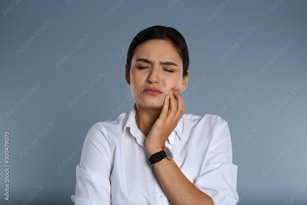 Woman suffering from toothache on grey background Woman suffering from toothache on grey background