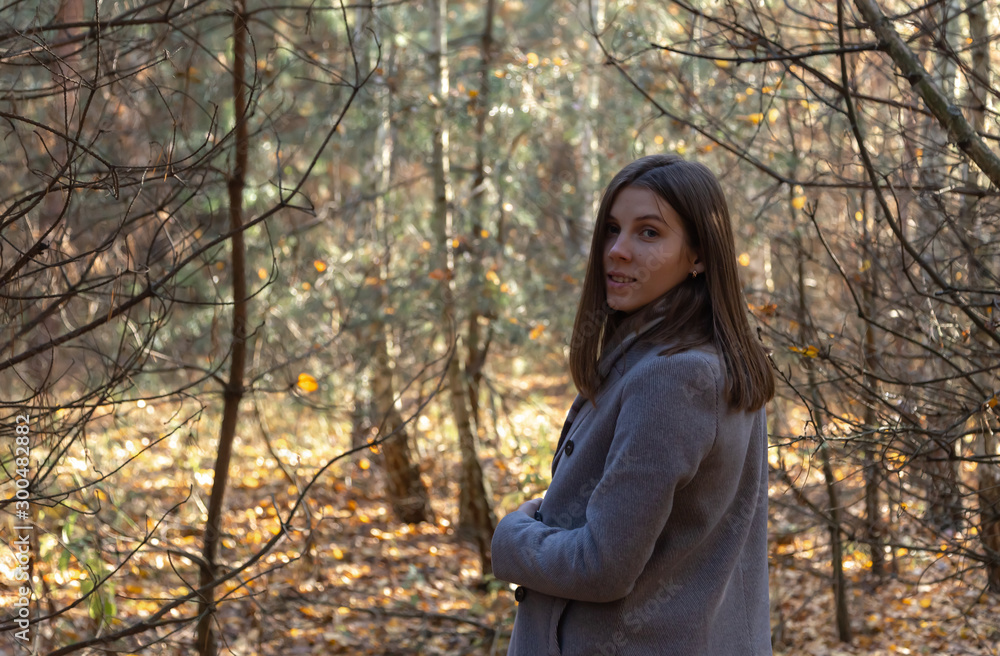 Half-turned girl in a gray coat, which stands in the forest on a sunny autumn day. Half-turned girl in a gray coat, which stands in the forest on a sunny autumn day.