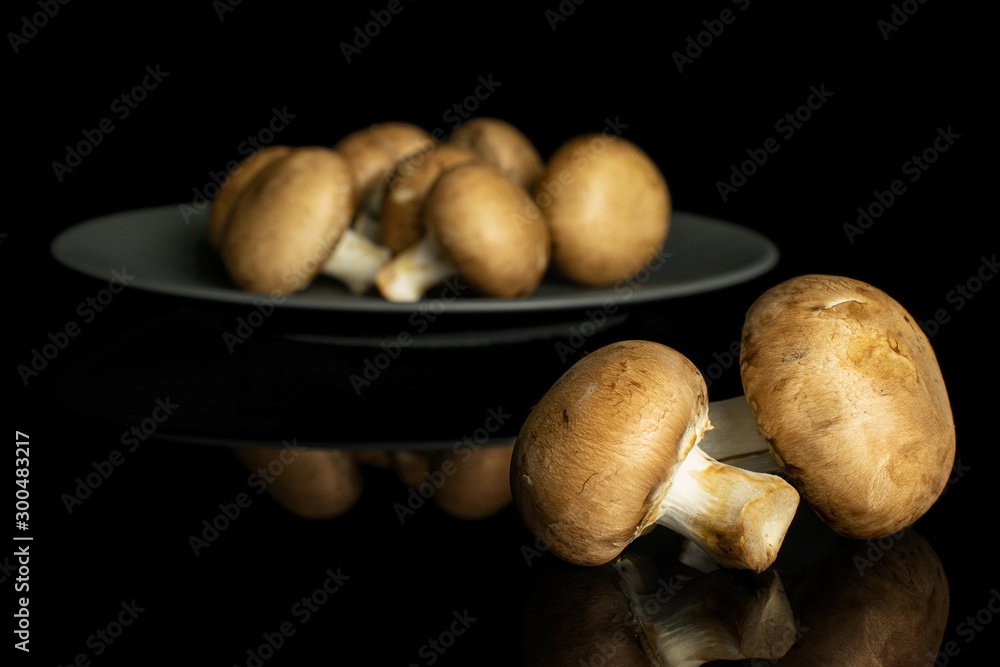 Lot of whole fresh brown champignon on gray ceramic plate isolated on black glass Lot of whole fresh brown champignon on gray ceramic plate isolated on black glass