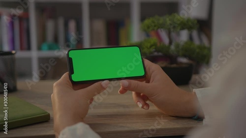 Young hands woman use smartphone phone with horizontal green screen sitting at desk technology internet sitting business device female home mobile app communication display holding slow motion