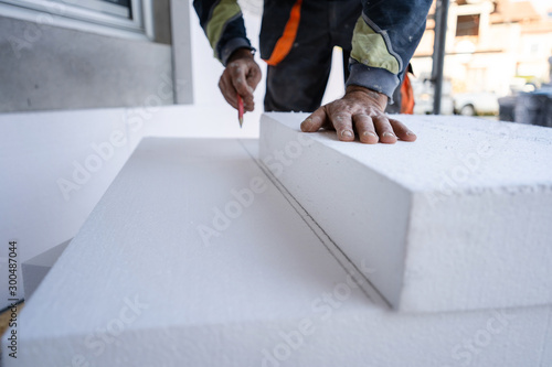 Worker use pen to mark the correct length and dimension of styrofoam during the wall insulation process at the construction site to cut the right size of the board photo