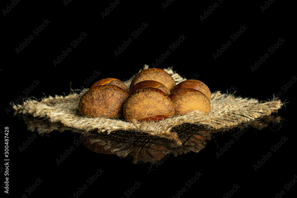 Group of seven whole sweet brown chestnut on natural sackcloth isolated on black glass Group of seven whole sweet brown chestnut on natural sackcloth isolated on black glass
