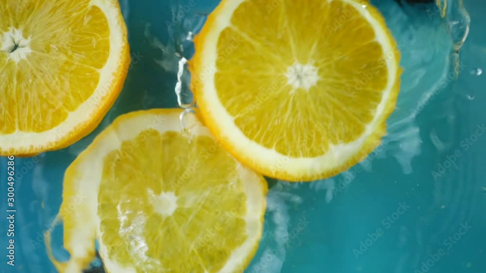 Orange fruit slice fall in water splash with drop water on blue background. Summer cold drink and fresh food concept Orange fruit slice fall in water splash with drop water on blue background. Summer cold drink and fresh food concept