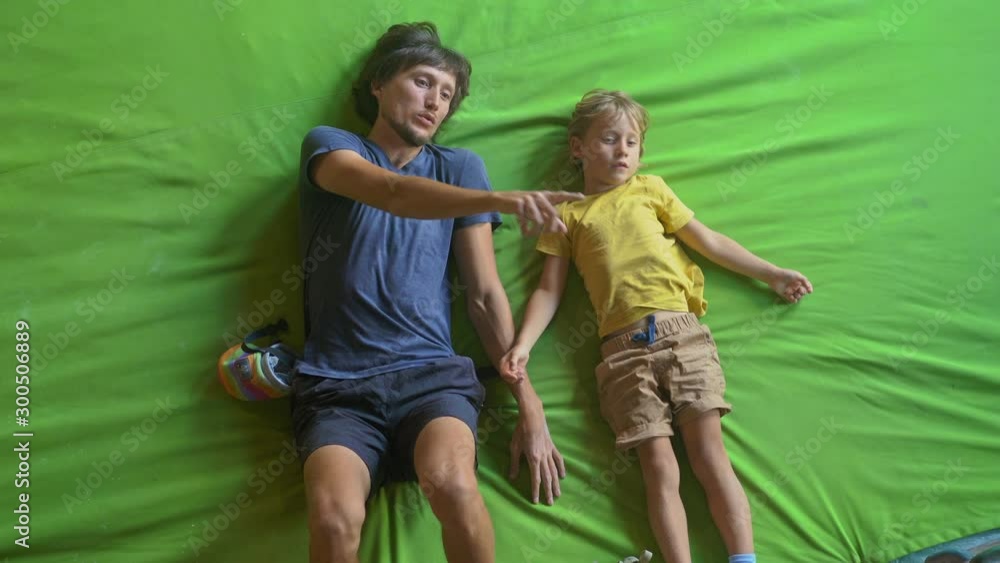 A young man climbing instructor teaching little boy how to climb the wall in a bouldering climbing gym A young man climbing instructor teaching little boy how to climb the wall in a bouldering climbing gym
