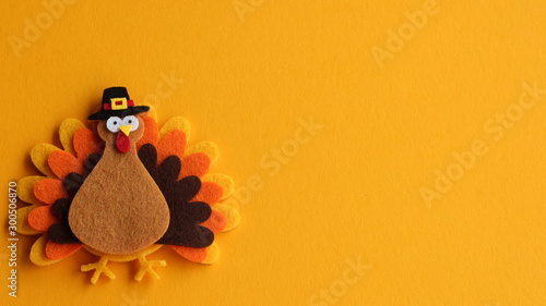 orange brown and yellow crafted felt turkey laying flat on an orange background with copy space	 photo