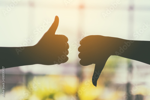 Silhouette image of two hands making thumbs up and thumbs down sign photo