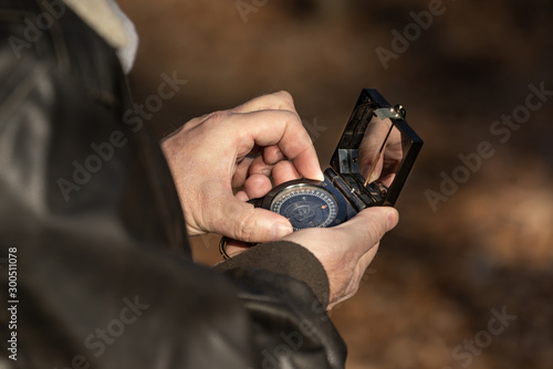 Older white outdoorsman Caucasian man with rough manly hands uses old wwii style analog magnetic military compass to find his way through the woods non GPS route finding photo