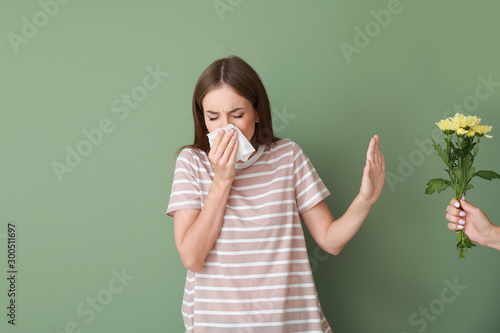 Young woman with allergy refusing to take bouquet on color background photo