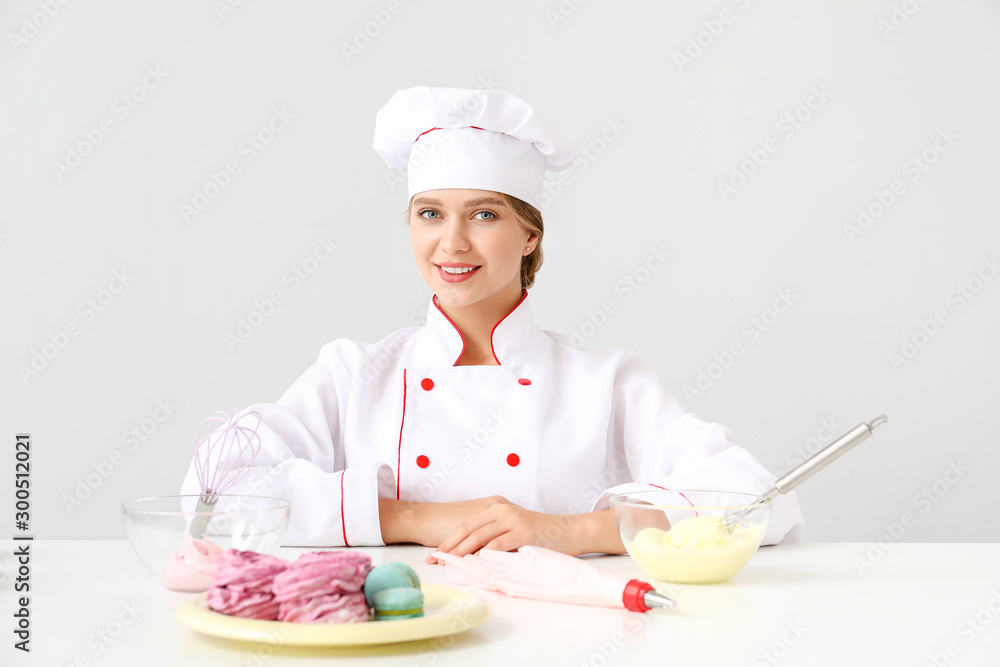 Female confectioner with tasty desserts on light background