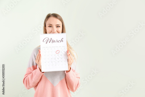 Beautiful young woman with calendar on light background. International Women's Day celebration