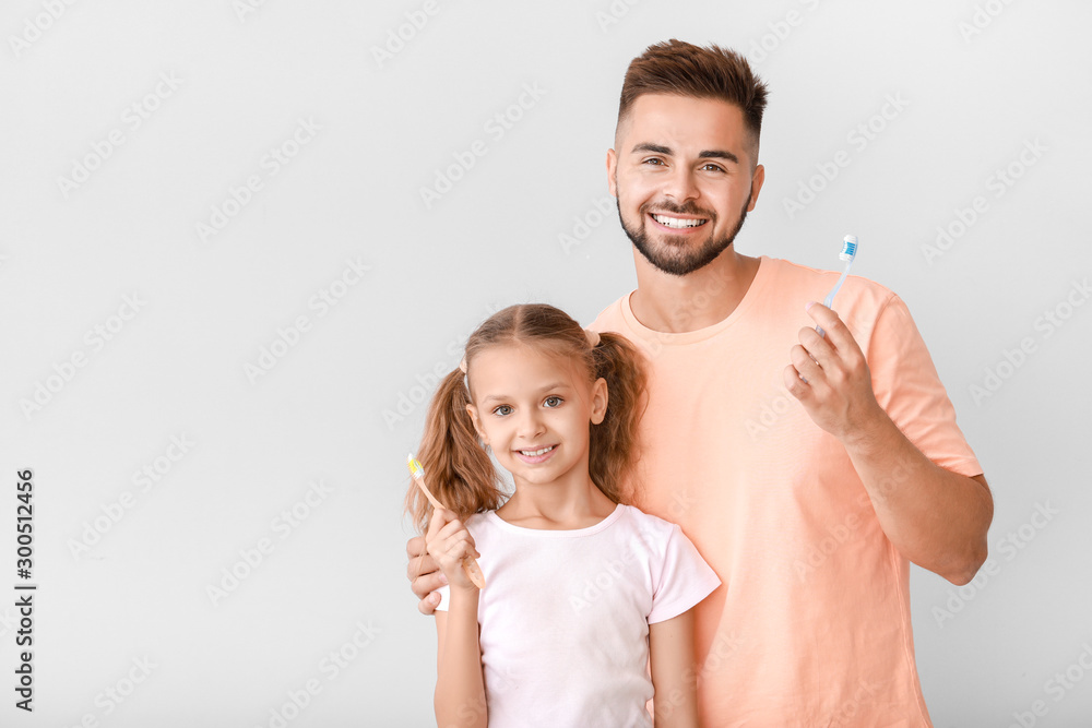 Portrait of man and his little daughter brushing teeth on light background Portrait of man and his little daughter brushing teeth on light background
