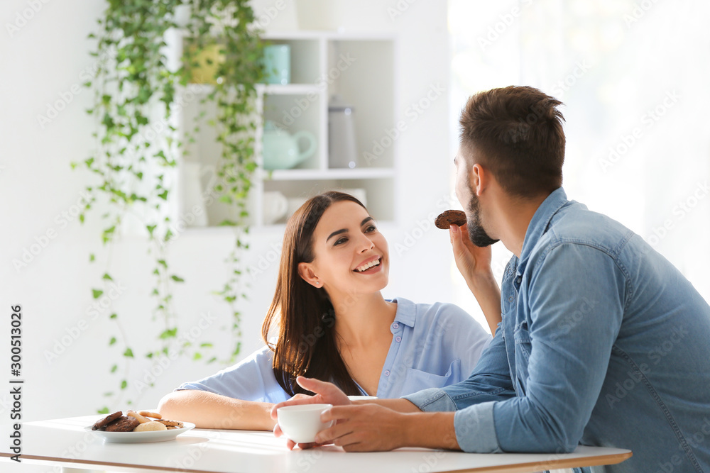 Fototapeta premium Happy young couple drinking coffee with cookies in kitchen at home