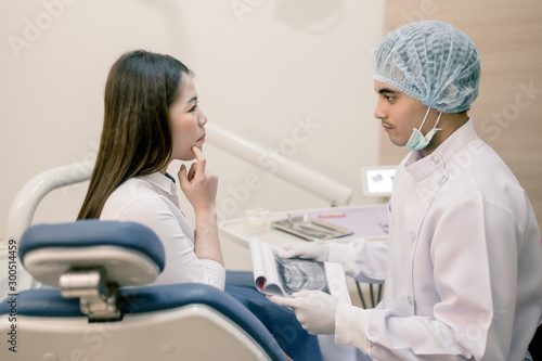 Happy dentist and patient commenting treatments in a tablet application in a consultation with medical equipment in the background