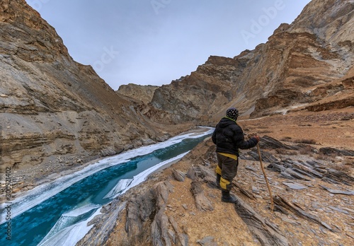 wanderlust trekker standing by a lake with blue water surrounded by dry brown mountains in Chadar