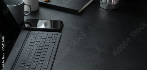 Close-up view of dark trendy workplace with smartphone, laptop computer and office supplies