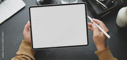 Close-up view of man using blank screen tablet while working in dark modern workplace