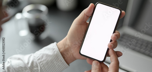 Cropped shot of professional businessman holding blank screen smartphone in dark modern office