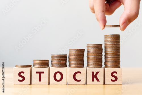 Hand putting coins on stack stair as step growing growth and wooden cube block with word STOCKS. Investment and save money concept