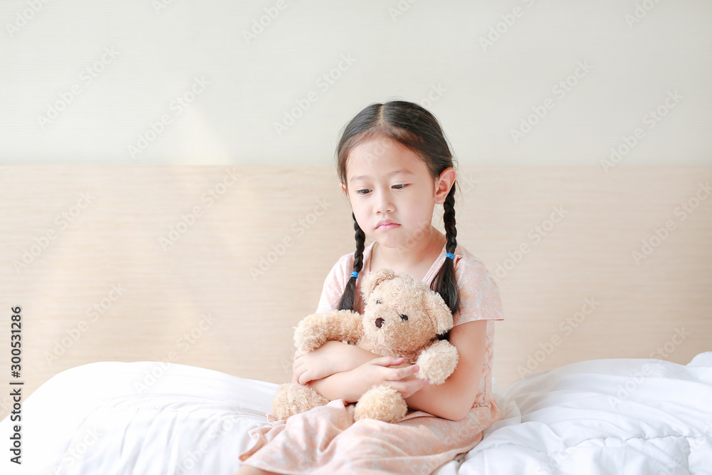 Peaceful Asian little girl embracing teddy bear while sitting on the bed at home. Peaceful Asian little girl embracing teddy bear while sitting on the bed at home.