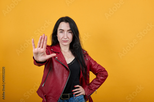 Portrait of serious young woman in casual clothes showing stop gesture with palm isolated on yellow wall background in studio. People sincere emotions lifestyle concept.