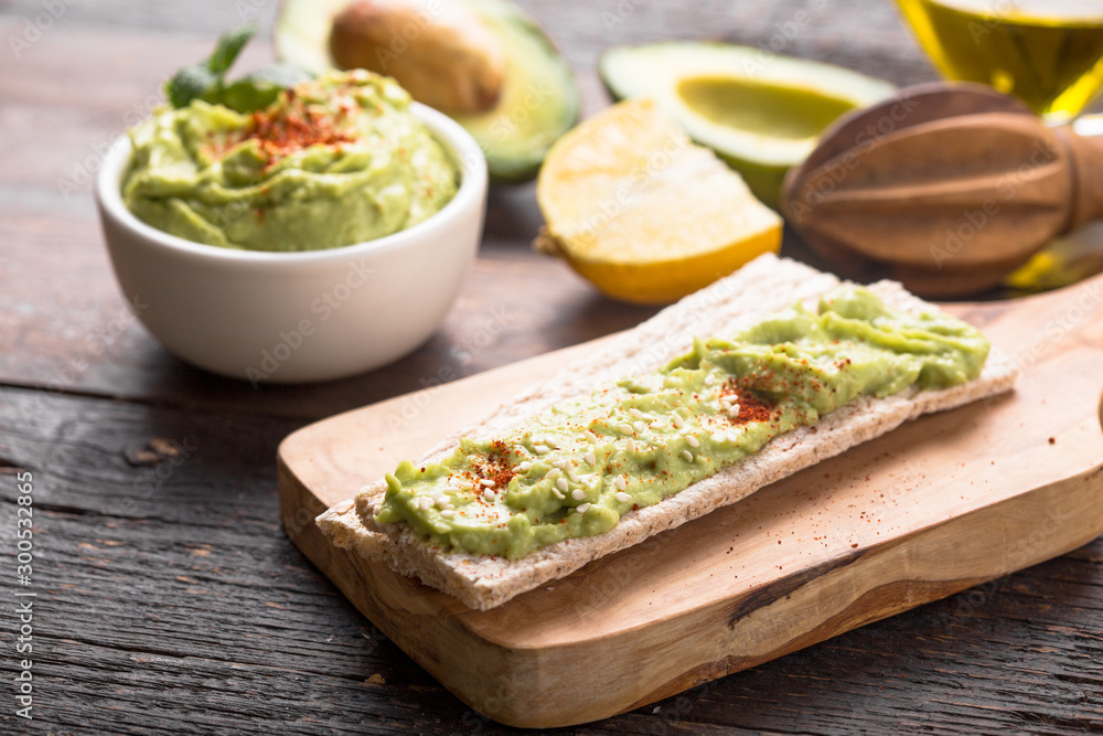 Two crackers with green  hummus, delicious cream of chickpeas and avocado on a wood background.