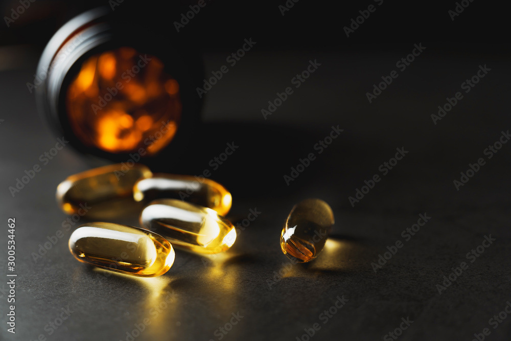 Macro photo of Omega 3 capsules and a derk glass jar on a black background. Low key photo. Medicine, healthcare and pharmacy concept. Macro photo of Omega 3 capsules and a derk glass jar on a black background. Low key photo. Medicine, healthcare and pharmacy concept.