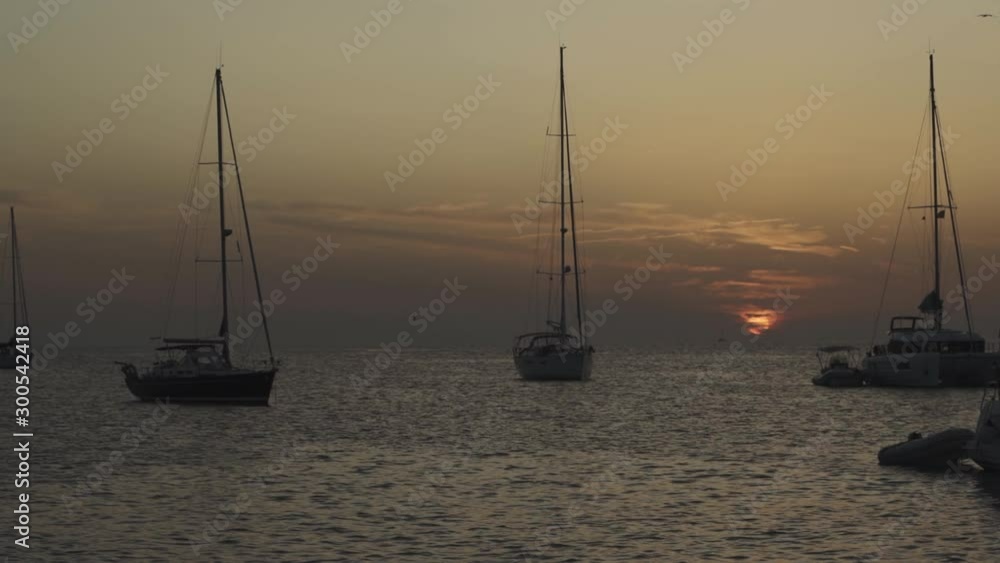 Many yachts in a bay on Formentera island. Incredible sunset in Cala Saona bay. Silhouettes of unrecognizable people on yachts Many yachts in a bay on Formentera island. Incredible sunset in Cala Saona bay. Silhouettes of unrecognizable people on yachts