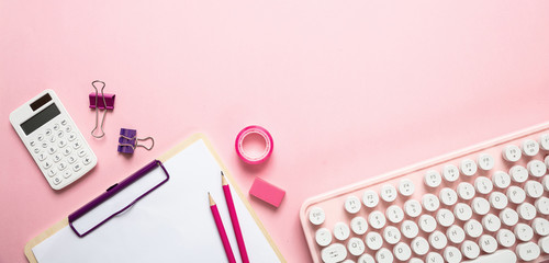Computer keyboard and office supplies against pink background