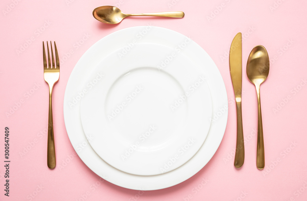 Gold cutlery and dishes set against pink background, formal place setting - obrazy, fototapety, plakaty 