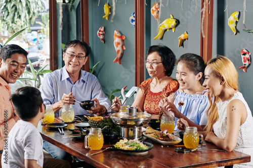 Happy big Asian family talking, laughing and eating good food at dinner