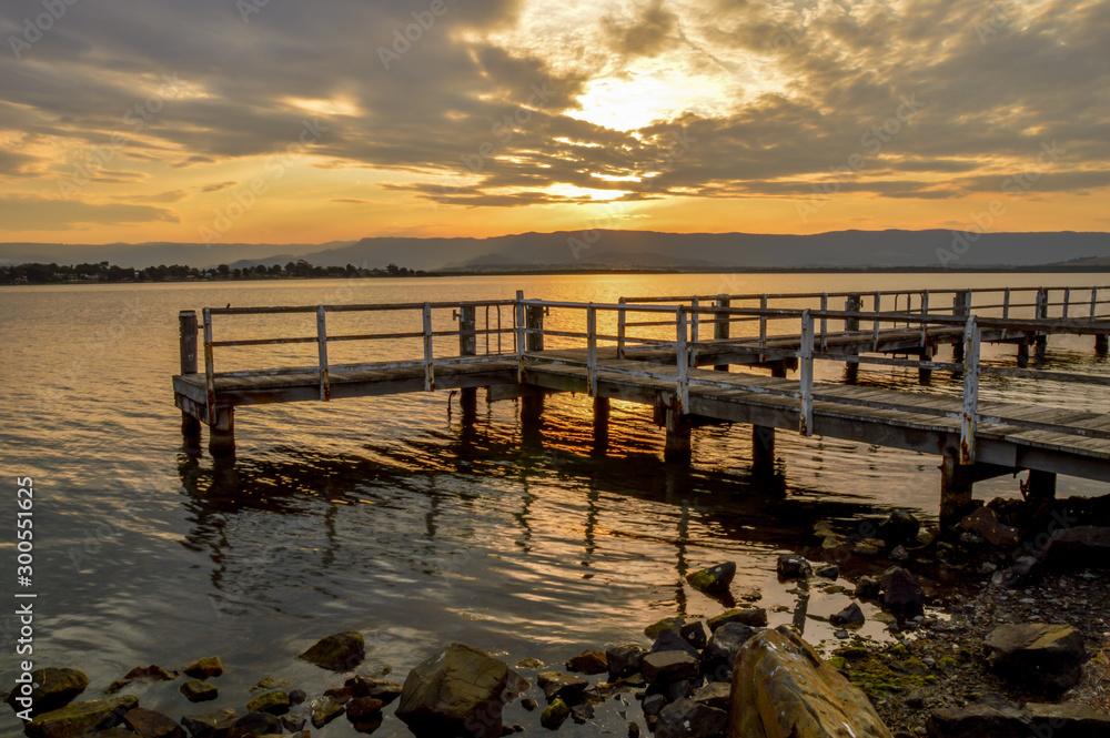 Obraz premium Old wooden jetty an sunset with rocks and water in foreground